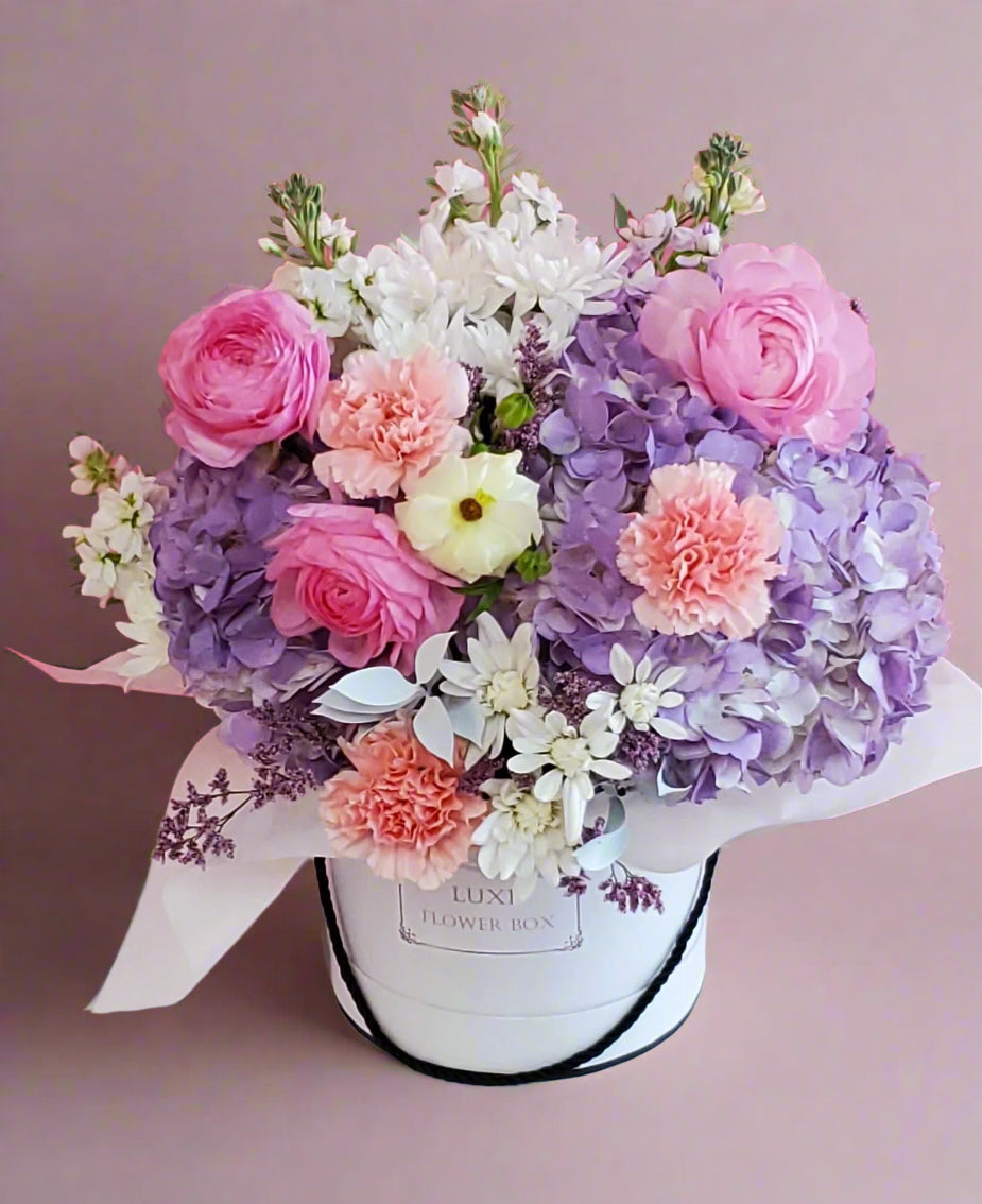 A luxurious flower box featuring a harmonious arrangement of ranunculus, carnations, and hydrangeas in soft, elegant tones, perfect for adding a touch of grace and beauty to any special occasion.