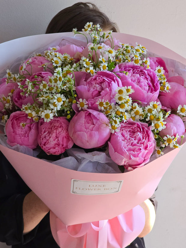 A delicate and romantic bouquet featuring lush peonies and cheerful chamomile flowers, creating a soft and charming arrangement perfect for adding a touch of elegance and whimsy to any occasion.