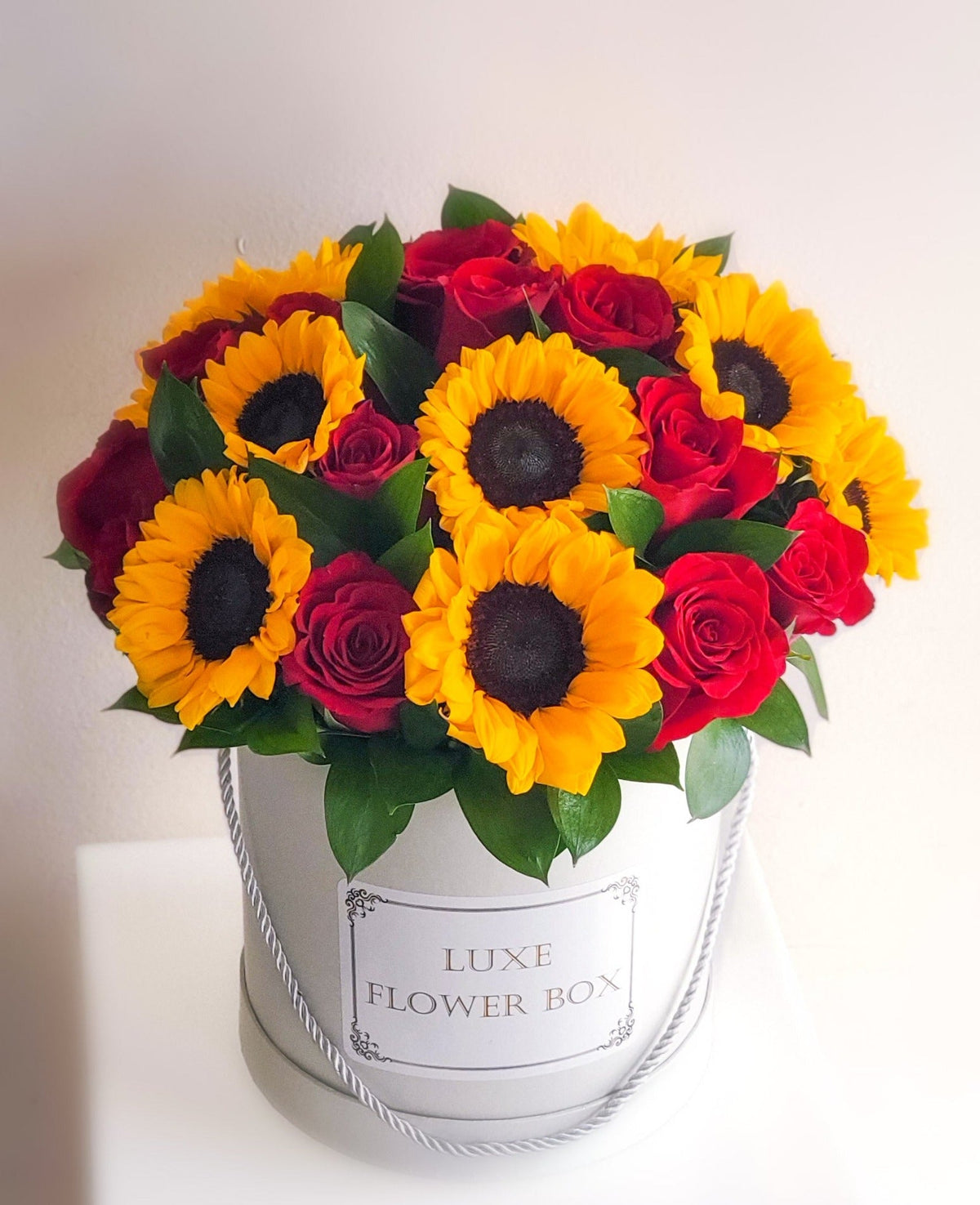 A vibrant flower box showcasing bold sunflowers and rich red roses, arranged beautifully to capture the warmth and passion of a sun-kissed day, perfect for brightening any occasion.