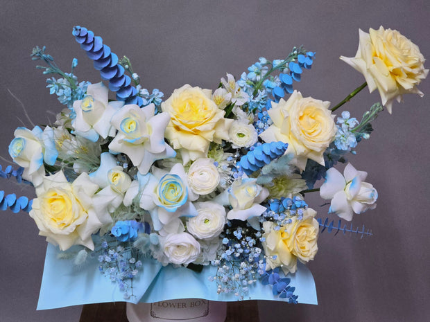 White and blue flower arrangement featuring Candlelight roses, white ranunculus, eucalyptus, and a touch of baby's breath in a delicate design