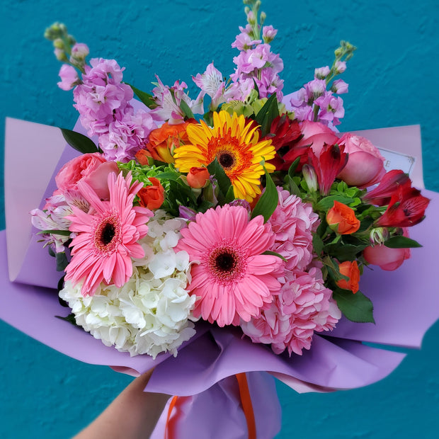 A captivating Charmin Blush Bouquet showcasing Gerbera daisies, lush hydrangeas, delicate garden roses, vibrant alstroemeria, fragrant stock flowers, and charming spray roses, elegantly arranged in soft blush tones with hints of greenery for a romantic and timeless look.